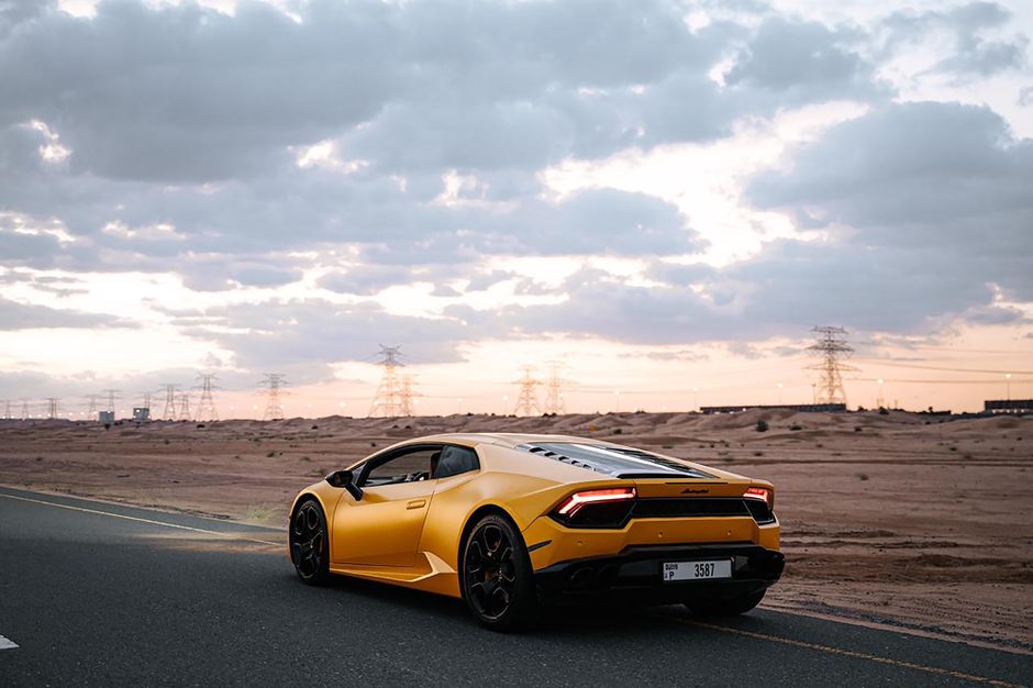 A yellow Lamborghini Huracan cruising on a scenic desert road at sunset with a dramatic sky.